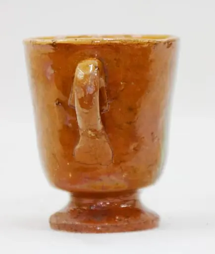 Piesa de formă relativ cilindrică, cu picior de susținere scund și toartă. Decorul este realizat prin pictare cu motive liber desenate (linii verticale). Cromatică: maro - roșcat (fondul), alb, verde, maro închis (decorul).