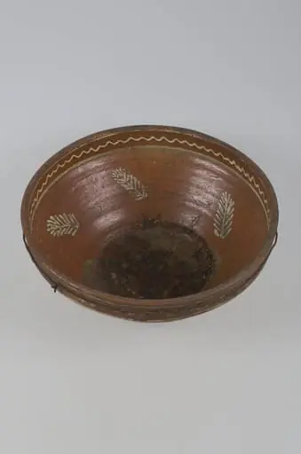 Vas adânc cu buza dreaptă, smălțuit în interior și pe exterior. Decorul este plasat pe buză (interior și exterior) format din motive geometrice: linia frântă. În interior, pereții sunt decorați cu frunze iar fundul cu frunze și flori. Cromatică: fond: brun; motive; alb; verde.