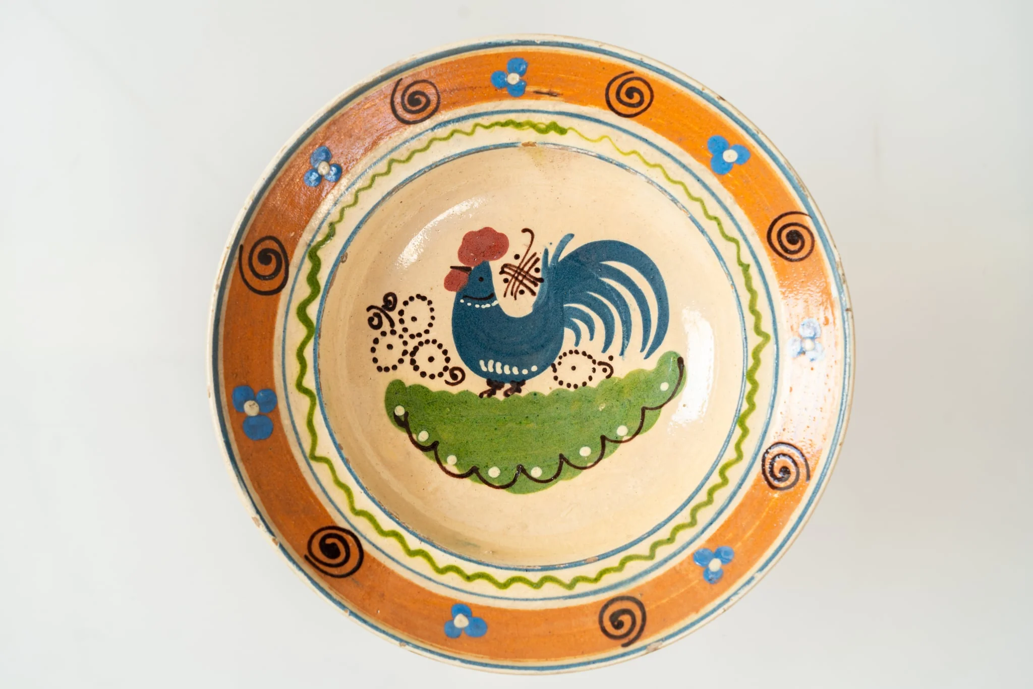 Formă adâncă, cu buză lată, răsfrântă. Piesa este modelată la roată, angobată cu humă albă. Decorul este realizat prin pictare cu pensula și cu cornul. Decorul, dispus pe întreaga suprafață a farfuriei, este format dintr-un motiv avimorf (cocoș, în zona centrală a farfuriei), motive florale și vegetale stilizate (central și pe buză) și motive geometrice (puncte, linii sub formă de cerc, linie vălurită, linie spiralată). Fața interioară a farfuriei este smălțuită cu un smalț transparent, lucios. Cromatica: alb, verde, albastru, brun, maro, siena naturală., by Unknown, 1850