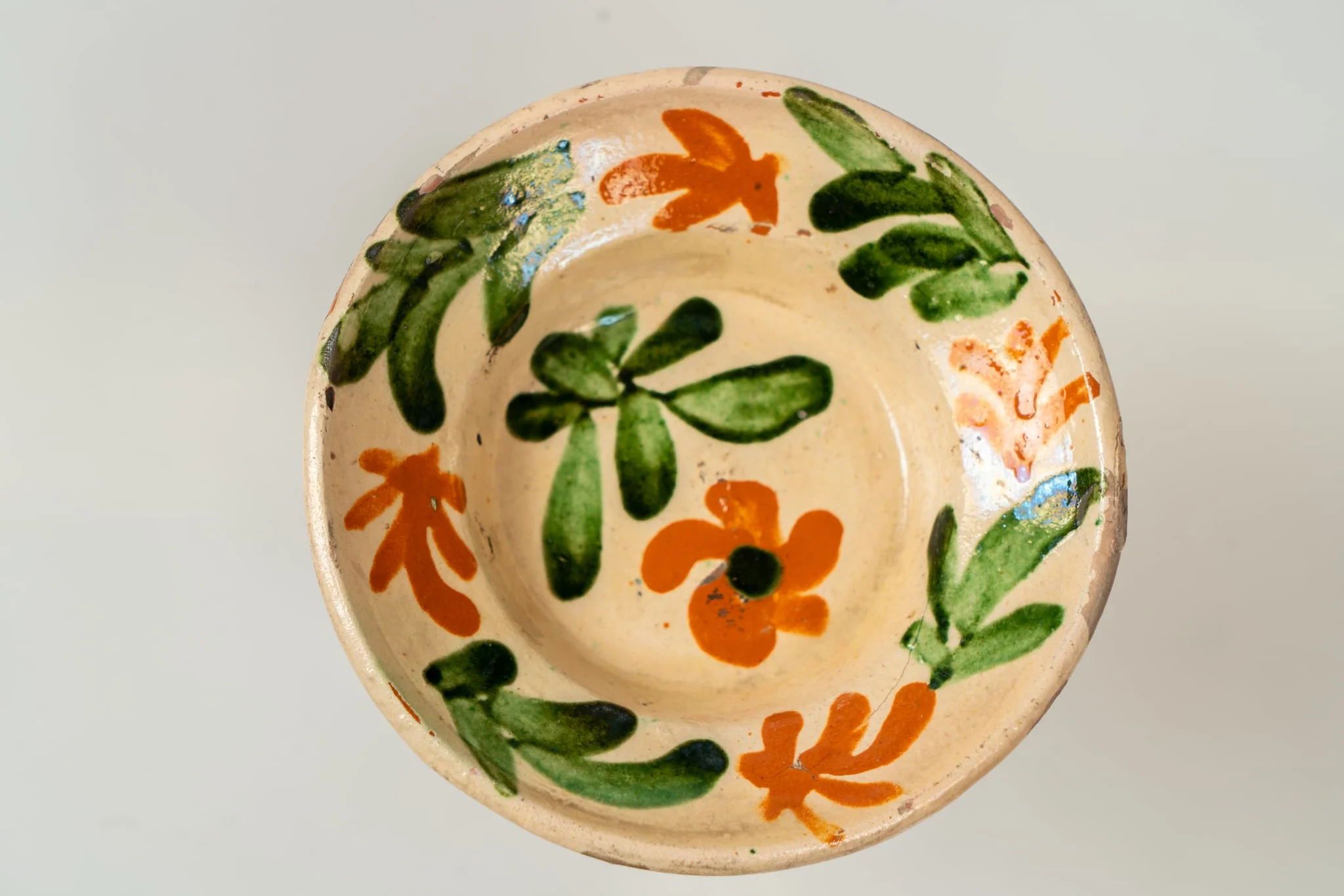 Farfurie mică, adâncă, cu buză răsfrântă. Piesa este modelată la roata olarului, angobată. Decorul este realizat prin pictare cu pensula și constă în motive decorative florale și vegetale (flori și frunze), dispuse central, pe fundul farfuriei și pe toată buza acesteia, sub formă de ghirlandă. Cromatica: alb, verde, siena naturală. Farfuria este smălțuită pe interior, cu smalț transparent., by Unknown, 1850