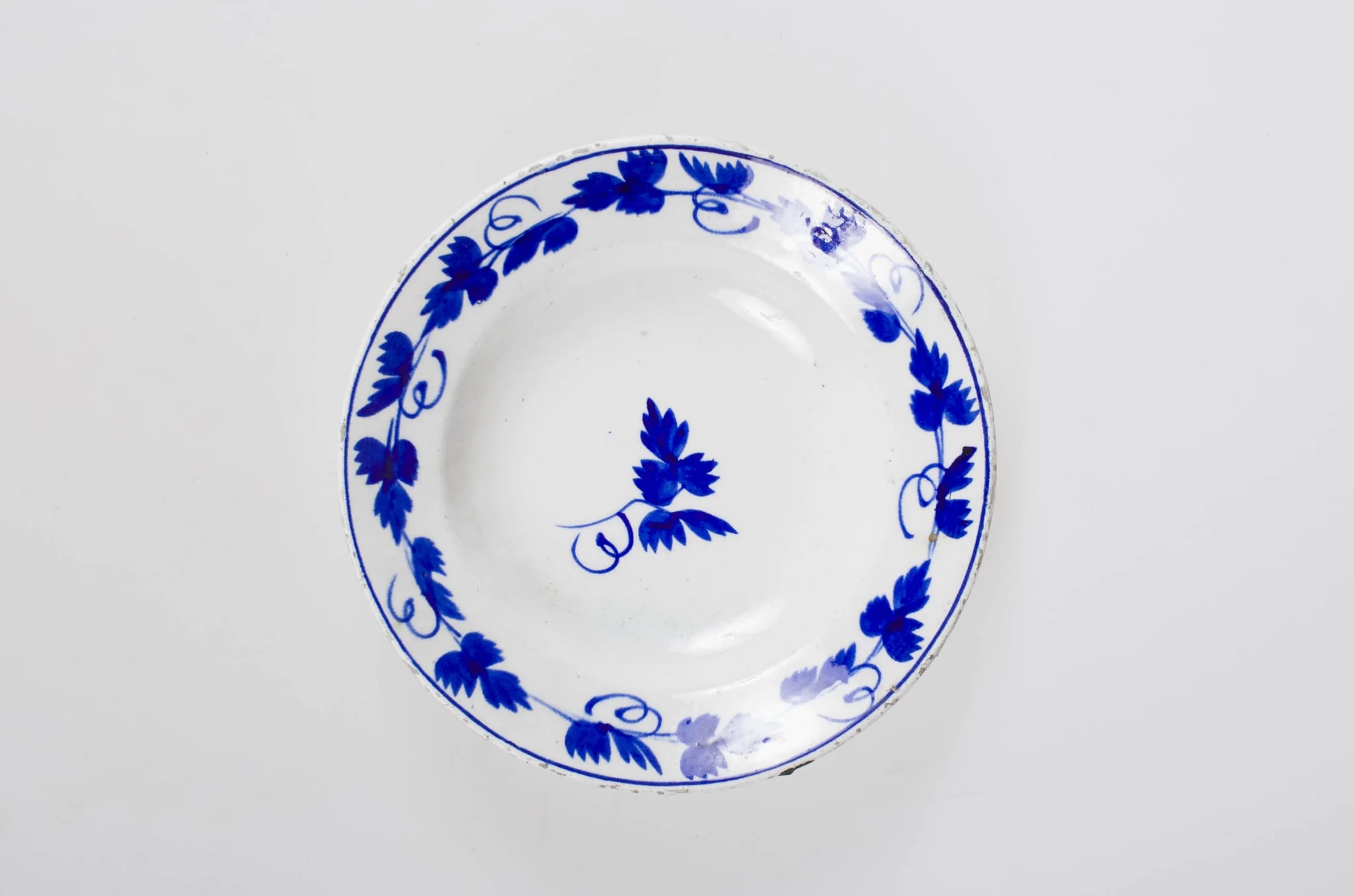 Obiect de uz casnic de formă tronconică. Pe fond alb se regăsește un ornament albastru: central două frunze de viță de vie. Pe margine farfuria este decorată cu frunze de viță de vie cu vrej și cu un cerc albastru. Cromatică: fond: alb; motive: albastru.