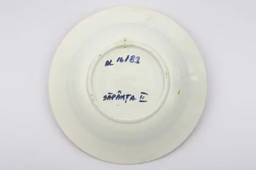 Vas ceramic de dimensiuni reduse, având formă tronconică, cu baza plată, pereții reficați și marginile evazate. Peste fondul alb au fost realizate decorațiile geometrizante și fitomorfe stilizate, dispuse în două registre. Primul registru este format dintr-un trandafir portocaliu cu frunze verzi, având în laterale câte o floare cu mijlocul albastru și petalele roșii, și câte un boboc roșu. Al doilea registru este format dintr-o tulpină circulară verde, pe care se dezvoltă trei grupuri de flori mici albastre. Alte trei grupuri, a câte trei linii portocalii oblice, însoțesc decorul fitomorf. Acest ultim registru este încadra dinspre interior de bandă groasă portocalie. Buza farfuriei a fost la rândul ei conturată cu portocaliu. Prezintă uzură funcțională. Cromatică: fond: alb; motive; portocaliu; verde; albastru.
