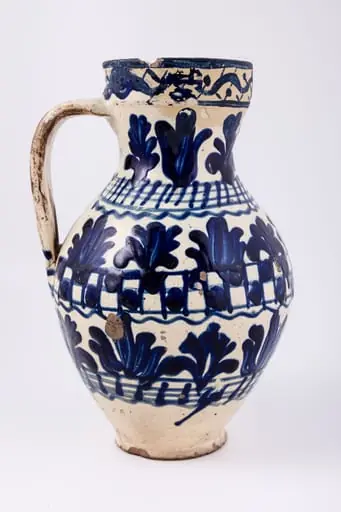 Cană piriformă prevăzută cu o toartă dreaptă și lată, gura rotundă. Suprafața decorativă a vasului este împărțită în șapte registre decorative: cel din partea superioară, pe buza vasului este dispus orizontal, iar celelalte șase, dispuse vertical. Primul registru, așezat pe marginea dreaptă a cănii redă o linie vălurită intercalată de puncte. Registrul al doilea, al patrulea și al șaselea prezintă motive fitomorfe și florale, brăduți intercalați de lalele înflorite stilizate. Registrul al treilea, dispus pe gâtul cănii și al șaptelea, dispus la bază, prezintă linii circulare orizontale intersectate de linii verticale. Registrul al patrulea prezintă tabla de șah. Toarta este pictată cu pensula. Cromatica: alb, albastru-cobalt.
