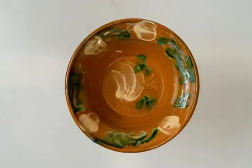 Farfurie mică, adâncă, de formă tronconică, cu buză lată, răsfrântă. Piesa este modelată la roata olarului, nefiind angobată. Decorul este realizat prin pictare cu pensula și constă în motive decorative florale și vegetale (flori și frunze), dispuse central, pe fundul farfuriei și pe toată buza acesteia, sub formă de ghirlandă. Cromatica: alb, verde. Farfuria este smălțuită pe interior, cu smalț transparent.