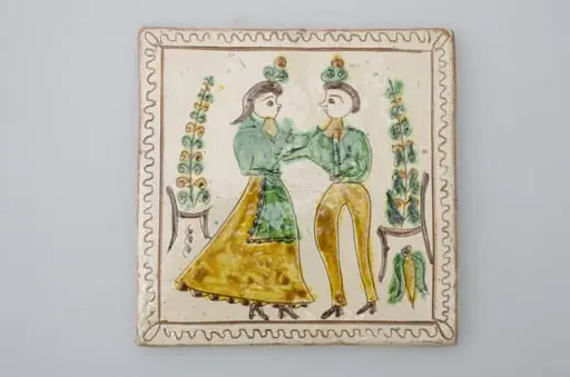 Piesă ceramică de formă pătrată, smălțuită și angobată, cu rol decorativ. Laturile pătratului sunt marcate de două chenare, primul vălurit, al doilea în linie dreaptă. Ornamentată cu motive antropomorfe și floral-vegetale: doi tineri, un băiat și o fată ținându-se pe după mijloc (băiatul cu mâna dreaptă, fata cu stânga). În spatele lor câte un scaun din care se înalță o floare. Motivele au fost la început incizate, iar apoi pictate. Pe spate, cahla este prevăzută cu un orificiu pentru prinderea aței. Tot aici, este inscripționat numele meșterului olar, "Colibaba". Cromatică: fundal alb; motive: verde, galben, cărămiziu, maro, negru.