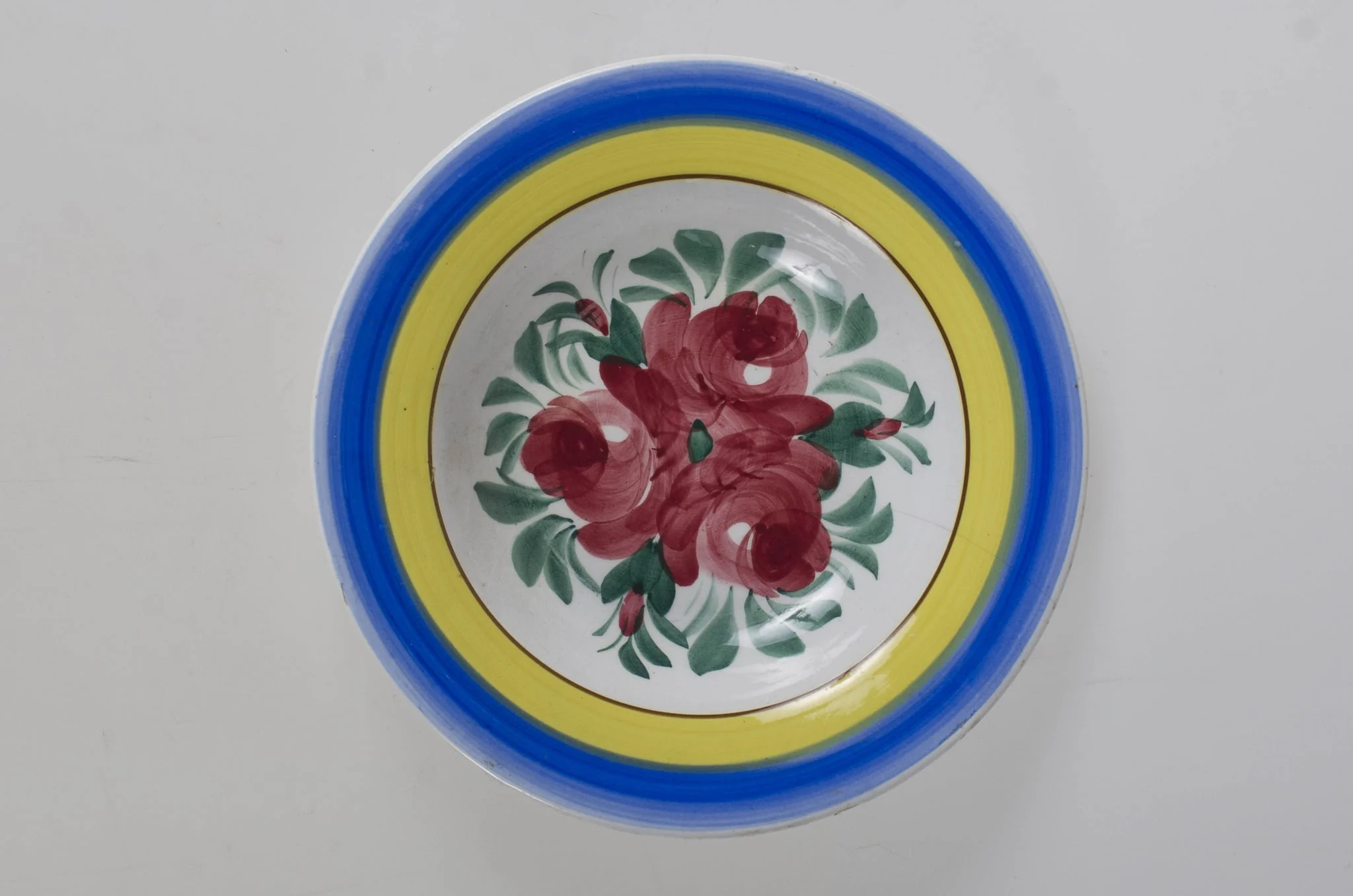 Farfurie de formă tronconică, adâncită; motive florale în centru (trandafiri); pe margine este decorat cu trei cercuri concentrice. Pe fund este o ștanță: o casă cu o pasăre pe acoperiș cu inscripție deasupra: ”MAGYAR” și dedesubt: ”1971” și un cuvânt indescifrabil. Pe fundul vasului sunt două incizii în care este introdus un șnur folosit la agățarea vasului pe perete. Vasul este smălțuit interior-exterior. Decor obținut prin pictare. Cromatică: fond: alb, motive: roșu; verde; albastru; galben., by Unknown, 1850