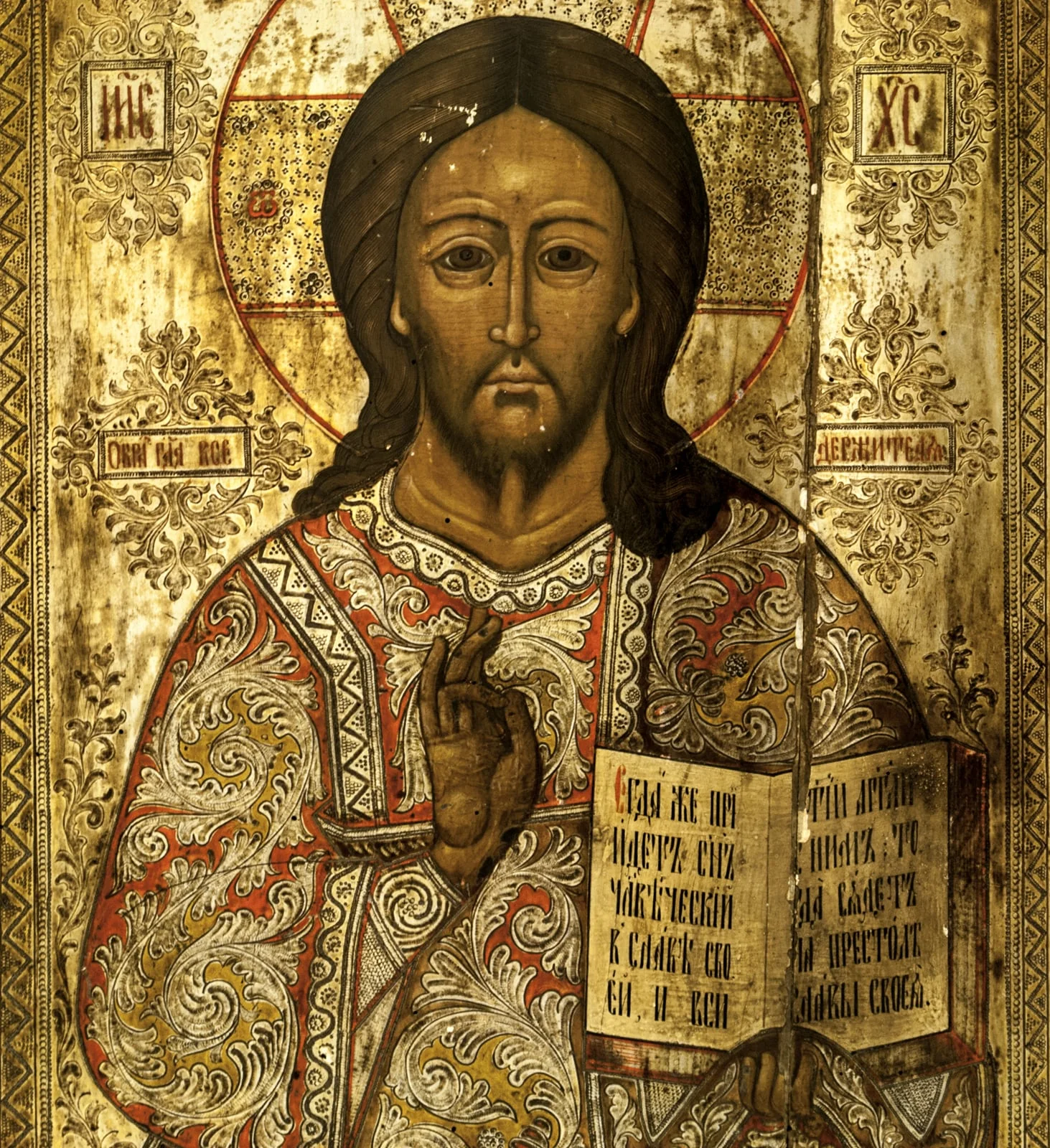Isus Pantocrator, redat 3/4, binecuvântând cu mâna dreaptă(prin unirea degetului mare cu cel inelar), în stânga ținând cartea sfântă cu textul consacrat, în slavonă(Veniți la mine toți cei oropsiți...).această reprezentare a lui Iisus binecuvântând, cu Evanghelia deschisă, corespunde în iconografia bizantină lui Iisus Învățător, sau Hristos Ușa, icoană amplasată în stânga ușilor împărătești. Conform erminiilor, Iisus Pantocrator este redat cu Evanghelia închisă.Expresia sobră, tristă, ochii mari, părul castaniu, lung, cu cărare pe mijloc, lăsat inegal pe umeri, mustățile și barba scurte. Poartă un veșmânt cu mâneci largi cu motive florale ample, în volute(foiță argintată), interstiții umplute cu portocaliu și galben. La mâneci, klav și la gât motive geometrice în formă de zigzag și val. Aureola (nimb cruciger) depășește spațiul chenarelor, trasată cu o linie de culoare roșie, dublată pe unele porțiuni cu o altă linie de culoare albă, în interior cu motive florale și puncte incizate în stratul de foiță metalică aurită. Inscripțiile consacrate: "eu sunt alfa și omega". Dublu chenar, motive geometrice: linii, puncte și zigzaguri între două linii fin incizate pe marginea foiței, la exterior bandă vișinie cu linii albe. Inscripțiile în chenare dreptunghiulare însoțite de motive fitomorfe incizate. Cromatica: alb, galben, roșu, auriu, brun, negru, foiță metalică; Bordura o înscrie în icoanele tip Krashnuska(înroșitele)., by Unknown, 1850