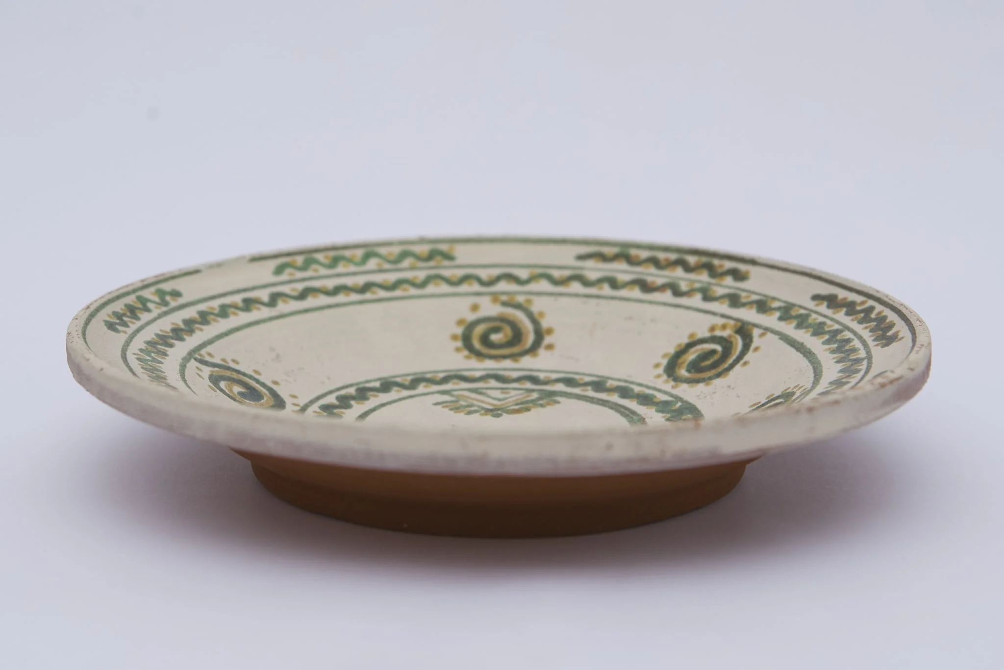 Vas ceramic de formă discoidală pe bază puțin înălțată. Fața farfuriei a fost introdusă în angobă albă, decorația a fost făcută cu pensula. Pe fundul vasului sunt două cercuri concentrice: în primul sunt doi brăduți, iar în al doilea valul punctat. Pe pereți sunt șase spirale punctate. Marginea vasului a fost împărțită în două registre, primul cu val punctat, în al doilea sunt șapte valuri întrerupte. La posterior, pe fund, semătura ”D Șchiopu ''. Pentru atârnare baza este perforată. Cromatică: fond: alb; motive; verde; galben., by Șchiopu Dumitru, unspecified