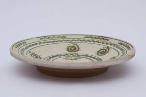Vas ceramic de formă discoidală pe bază puțin înălțată. Fața farfuriei a fost introdusă în angobă albă, decorația a fost făcută cu pensula. Pe fundul vasului sunt două cercuri concentrice: în primul sunt doi brăduți, iar în al doilea valul punctat. Pe pereți sunt șase spirale punctate. Marginea vasului a fost împărțită în două registre, primul cu val punctat, în al doilea sunt șapte valuri întrerupte. La posterior, pe fund, semătura ”D Șchiopu ''. Pentru atârnare baza este perforată. Cromatică: fond: alb; motive; verde; galben.