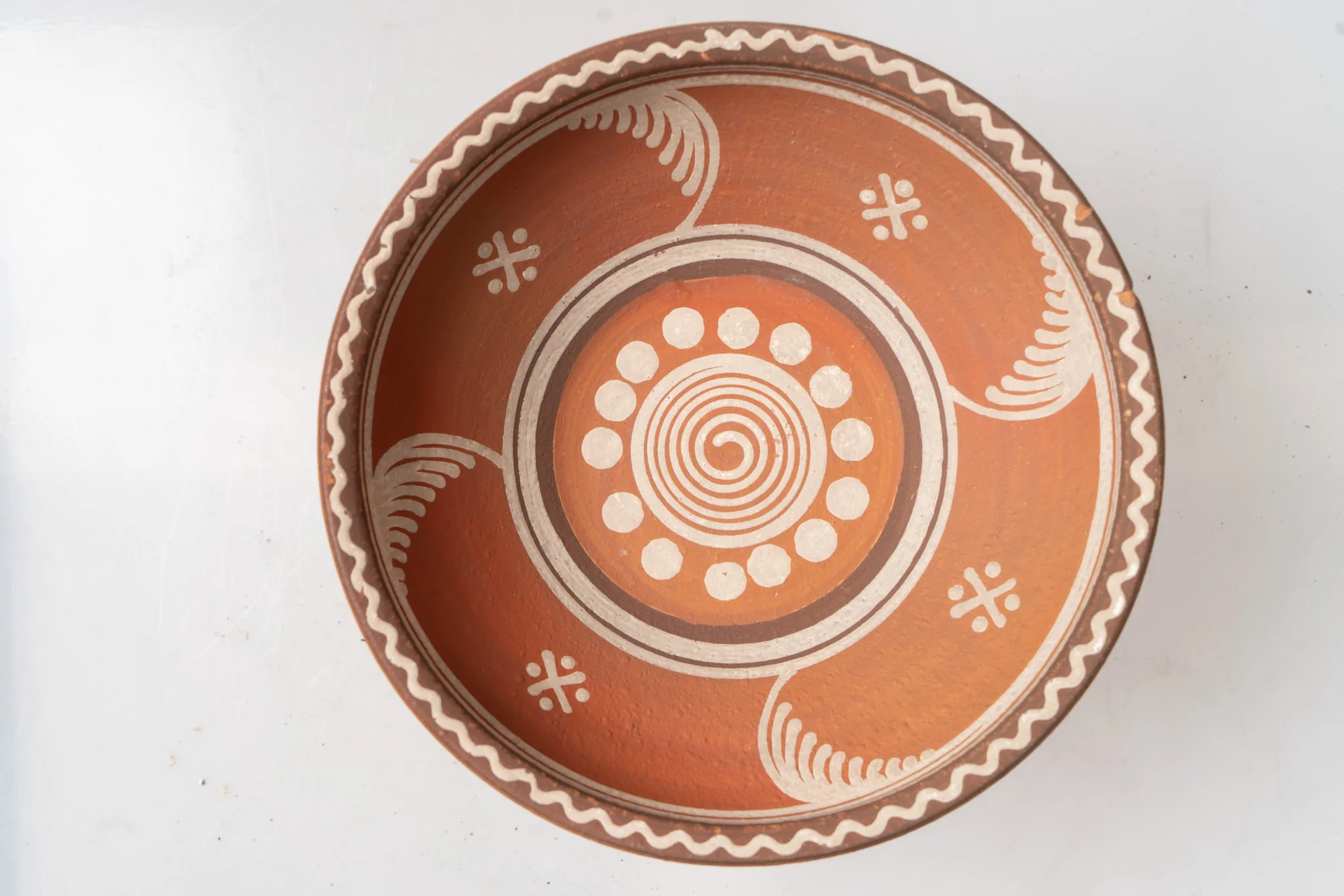 Farfurie adâncă de tip castron, cu corp tronconic, buză dreaptă și muchia buzei evazată; piesa este modelată la roata olarului nefiind angobată. Decorul este realizat cu angobă albă și maro-deschis, prin pictare cu cornul și cu pensula și se compune din motive geometrice (linie spiralată și puncte mari, albe, în registrul de pe fundul farfuriei; patru grupuri de linii paralele curbe, patru grupuri de linii intersectate sub formă de cruce, cu puncte între brațele acesteia, dungi maro-deschis, linii circulare albe, linie ondulată dispusă sub formă de cerc, pe peretele și buza farfuriei). Cromatica: maro-deschis, alb, pe fondul lutului ars. Farfuria este nesmălțuită., by Unknown, 1850