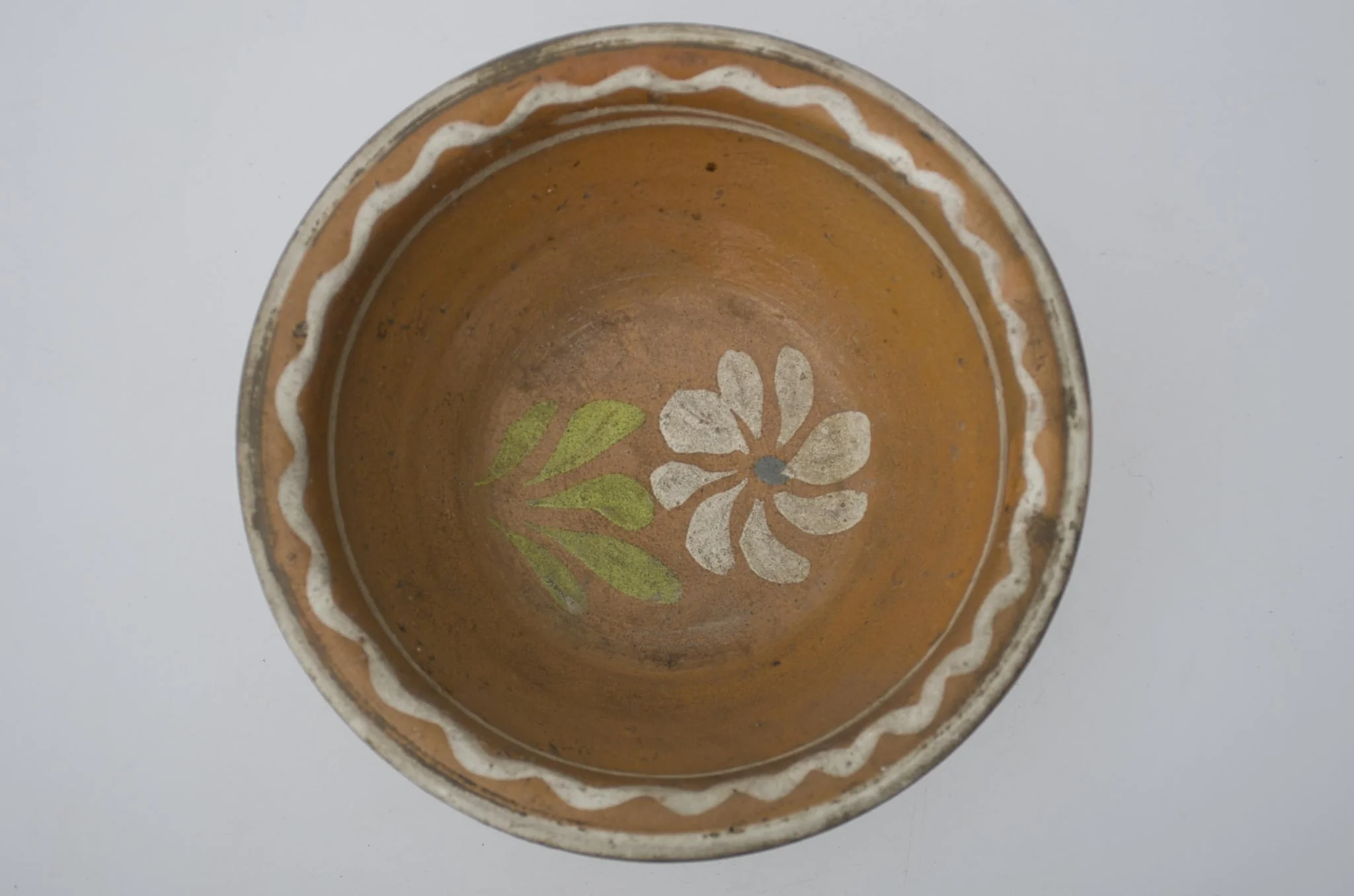 Farfurie adânca, de formă tronconică, smălțuită în interior. Pe margine prezintă decor geometric: linia vălurită; central o floare. Cromatică: fond: cărămiziu; motive: alb; verde; albastru., by Unknown, 1850