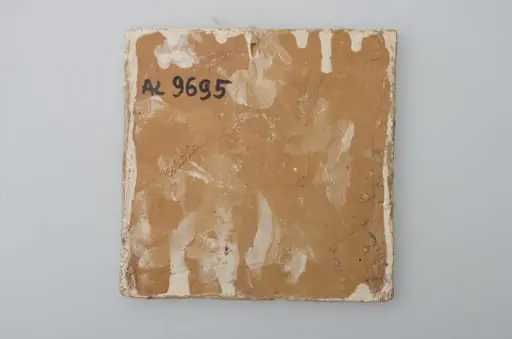 Piesă ceramică de formă pătrată, smălțuită și angobată, laturile pătratului fiind marcate de două chenare, primul vălurit, al doilea în linie dreaptă. Ornamentată cu motive zoomorfe și floral-vegetale, după fabula lui La Fontaine, Vulpea și barza: o vulpe care bea dintr-un ulcior și o barză care mânâncă dintr-un vas plat aflat pe o măsuță joasă. Pe două din colțuri, două flori completează pictura. Motivele au fost la început incizate, iar apoi pictate. Pe spate, cahla este prevăzută cu un orificiu pentru prinderea aței. Tot aici, este inscripționat numele meșterului olar, "Colibaba". Cromatică: fundal alb; motive: verde, galben, maro, cărămiziu.